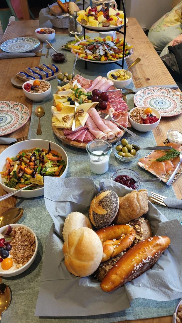 Reich gedeckter Frühstückstisch mit Wurst- und Käseplatte, Brotkorb und Müslischalen