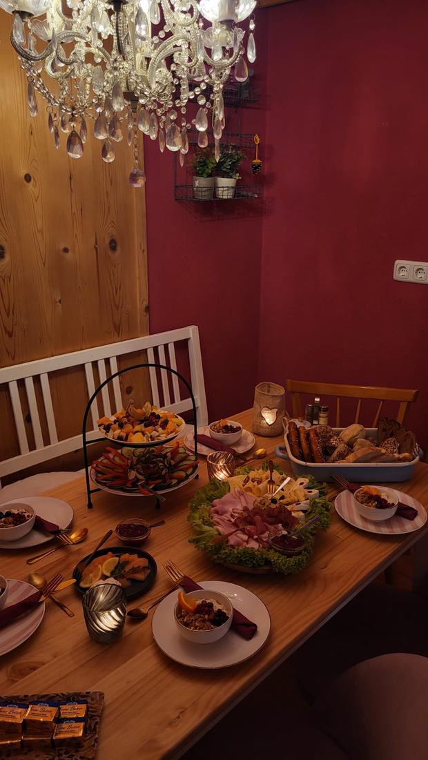 Gedeckter Frühstückstisch am Abend unter einem Kronleuchter, mit Etagere und Brotkorb