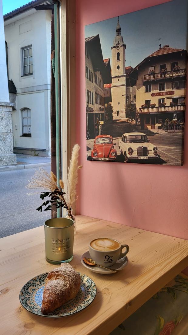 Fensterplatz mit Croissant und Cappuccino auf der Holztheke, dahinter die rosa Wand mit einem Bild vom Miesbacher Marktplatz