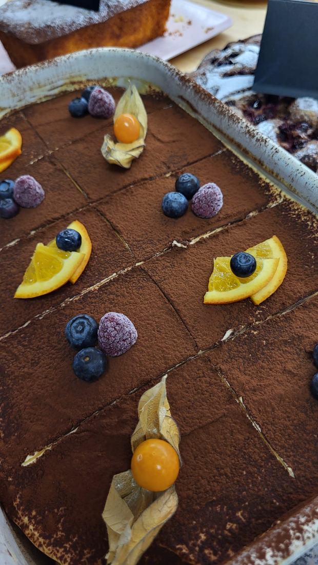 Blech mit Tiramisu, bestäubt mit Kakao und garniert mit Beeren, Orangenspalten und Physalis