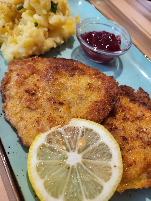 Paniertes Schnitzel mit Kartoffelsalat, Preiselbeeren und einer Zitronenscheibe
