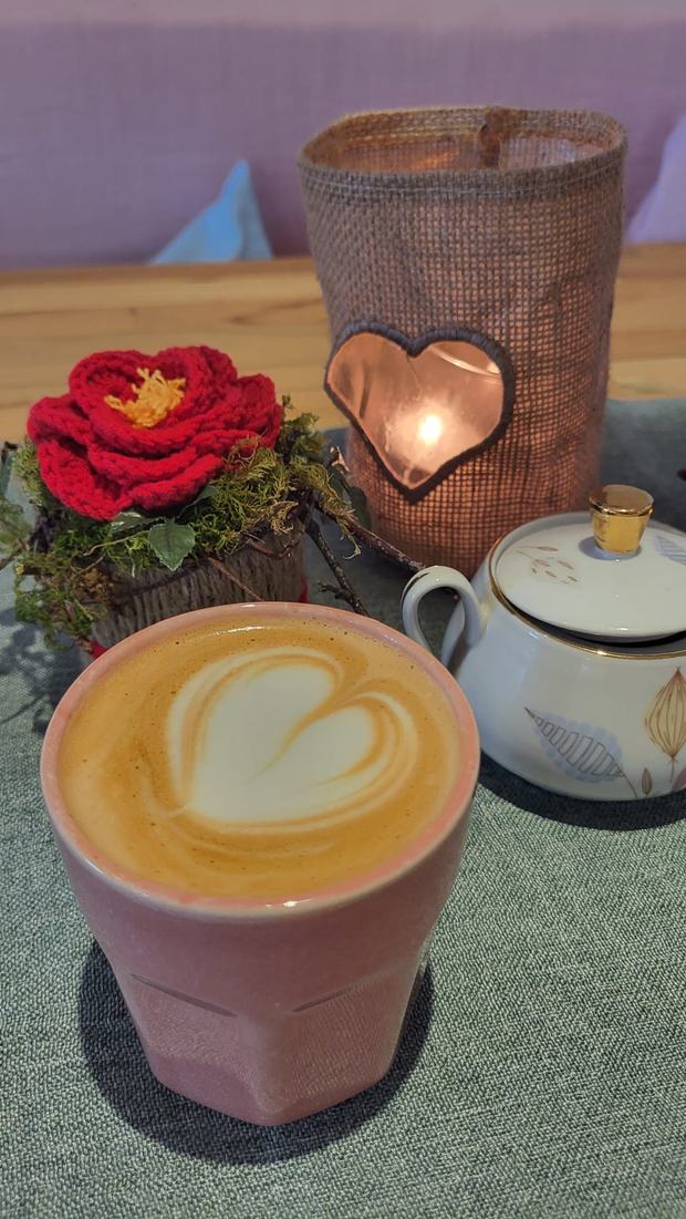 Cappuccino mit Herz im rosa Becher, daneben eine gehäkelte Rose und ein Windlicht