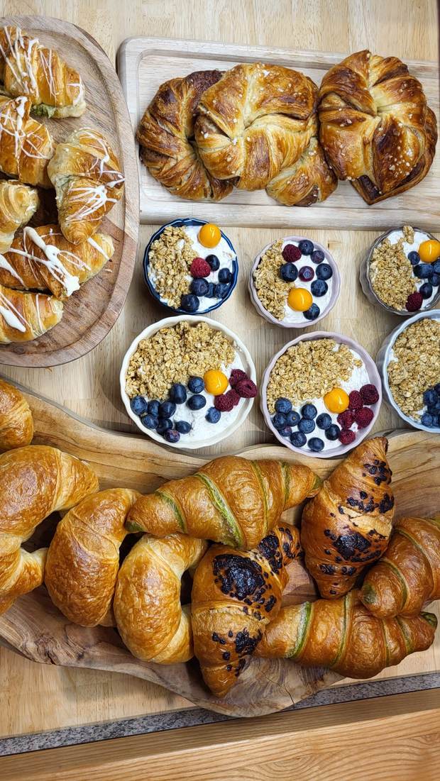 Holzbretter mit Croissants in mehreren Sorten und Schälchen mit Joghurt, Granola, Beeren und Physalis