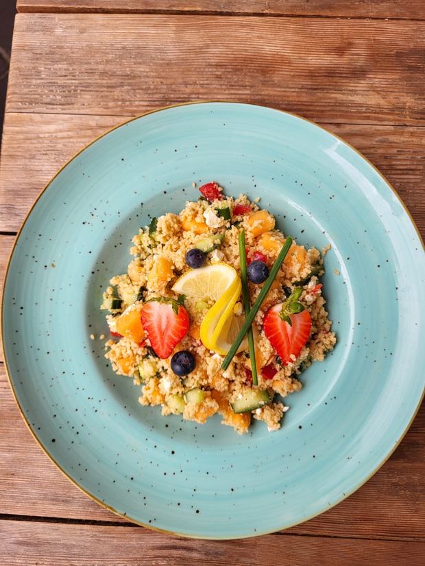 Couscous-Salat mit Gurke, Melone, Erdbeeren, Heidelbeeren und Feta auf einem türkisen Teller