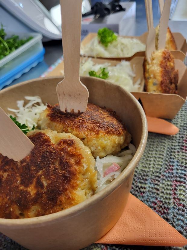 Goldbraun gebratene Kaspressknödel auf Krautsalat, angerichtet in Schachteln zum Mitnehmen
