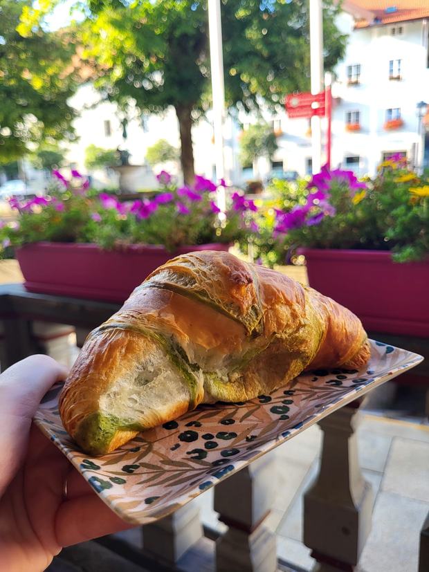 Matcha-Croissant auf einem gemusterten Teller, dahinter Blumenkästen und die Häuser am Miesbacher Stadtplatz